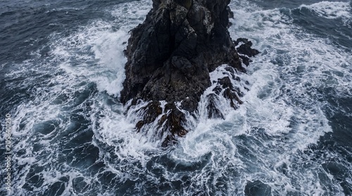 Aerial view of churning atlantic waves crashing violently around a dark jagged sea stack