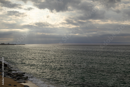 Sun Rays Through Clouds Over Calm Ocean and Rocky Coastline
