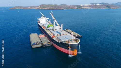 large bulk carrier ship transferring dark bulk cargo like coal or minerals into smaller barges alongside it in the open sea, representing maritime logistics and global supply chain.
