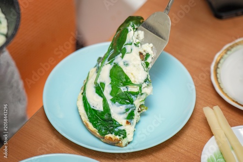 Serving a spinach omelette onto a blue ceramic plate using a metal spatula