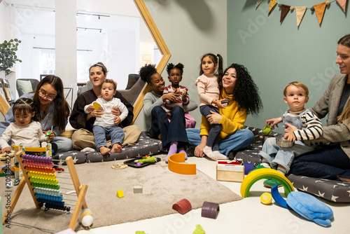 Diverse women with babies and toddlers sitting on floor playing with colorful toys