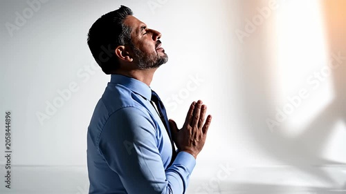 Man in blue shirt praying with hands together.