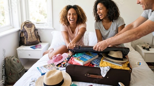 Happy family packing suitcase together for summer vacation in hotel room.