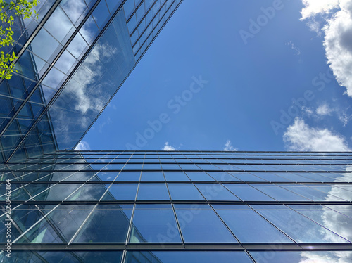 Looking up between two modern glass office buildings to a blue sky with clouds reflected in the windows