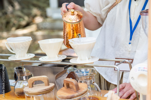 Foto 屋外のコーヒースタンドでドリッパーにお湯を注ぐ店員の手元、ドリップコーヒーをいれるカフェ店員　バリスタ