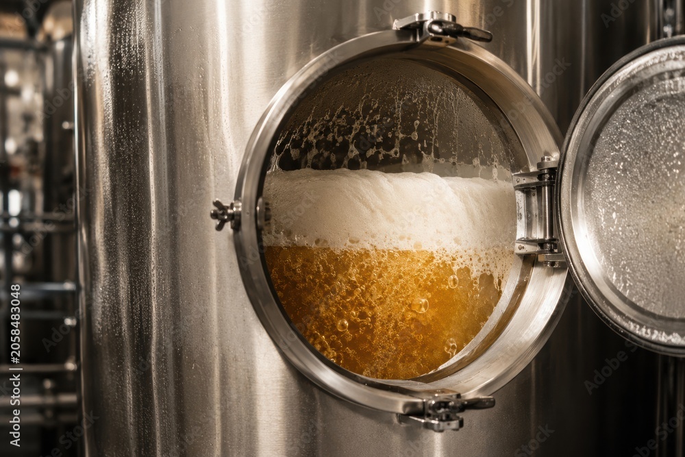 Obraz premium Beer fermentation process visible through glass window of stainless steel brewing tank in a modern brewery with bubbles and foam present
