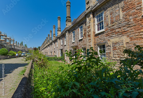 Quadro em tela A long row of historic stone houses with tall chimneys stands under a clear blue