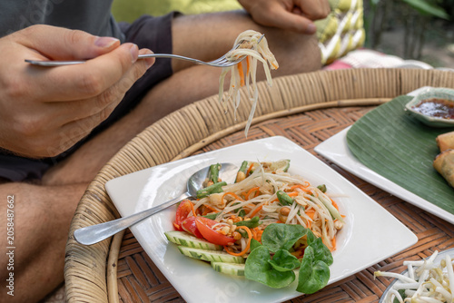 A person enjoys a delicious and healthy papaya salad (Som Tum) in a relaxed tropical setting, embodying the wellness and slow living aspects of a modern digital nomad lifestyle in Southeast Asia.