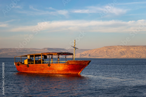 Foto Traditional wooden boat sailing on the calm blue waters of the Sea of Galilee un