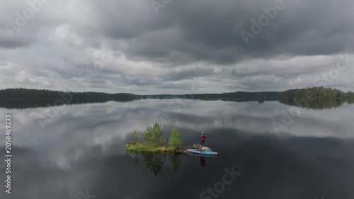 A lone kayaker takes a break on a tiny, secluded island in the middle of a calm wilderness lake. Aerial view of outdoor recreation and active lifestyle in Mujejärvi, Finland.