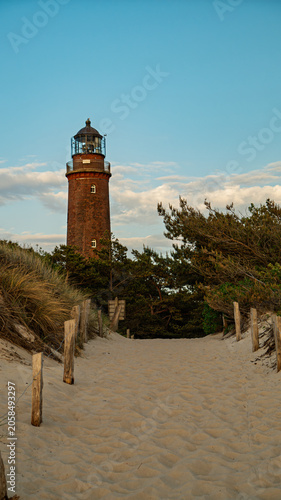 Sandy path with wooden posts leading to the historic red brick Darßer Ort Lighthouse, Germany.