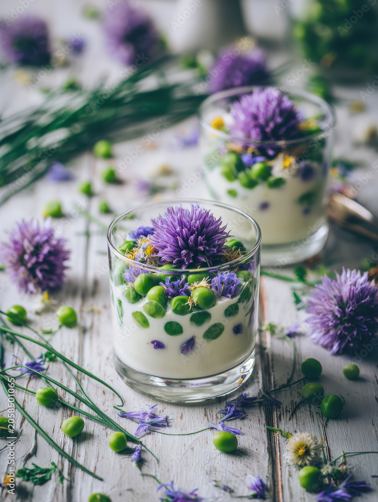 Fototapeta premium Fresh green peas pudding dessert with chive blossoms served in glasses on white rustic wooden table background, creative healthy vegan appetizers snack, beautiful summer seasonal food photography