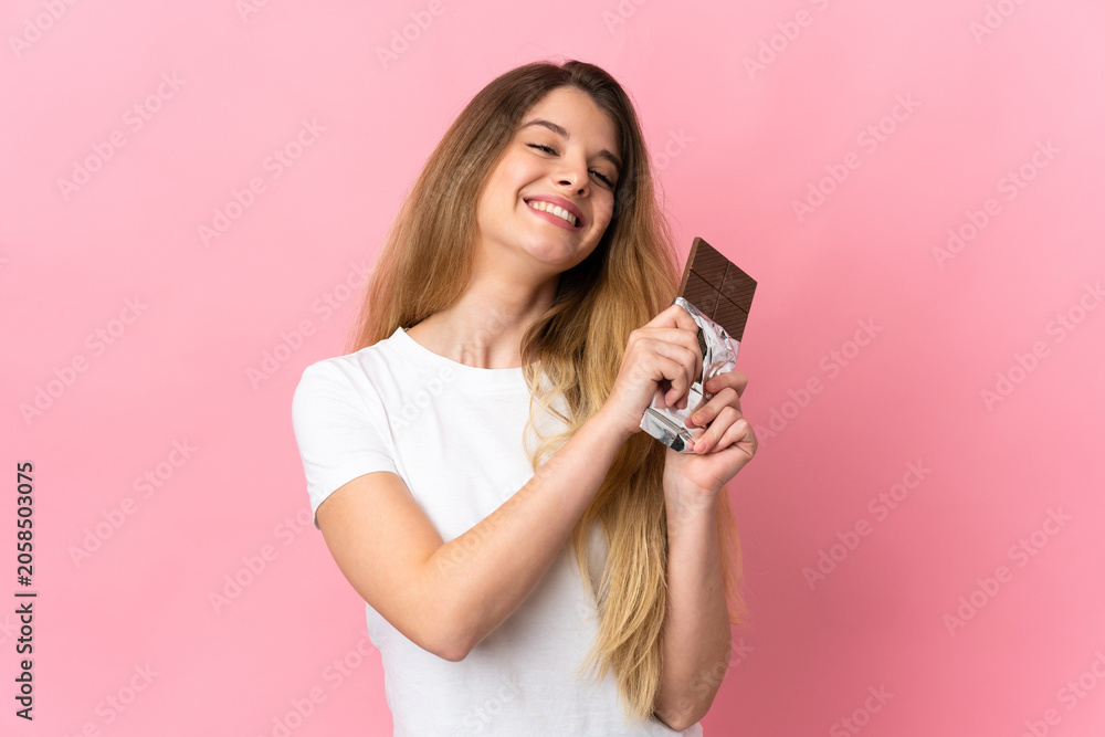 Fototapeta premium Young blonde woman isolated on pink background taking a chocolate tablet and happy