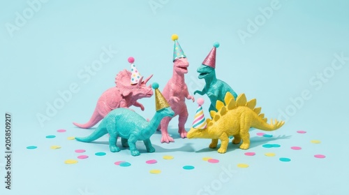Cute dinosaur toys wearing party hats celebrate with confetti on a pastel background