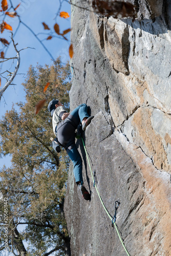 Dynamic Rock Climber Scaling Steep Granite Wall with Safety Rope on Clear Autumn Day