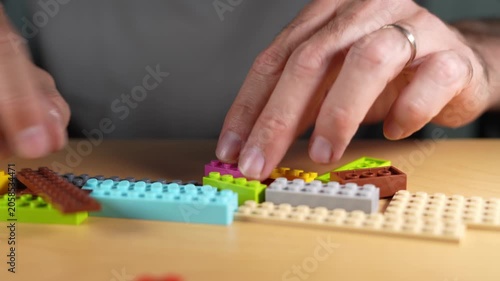 Creative man with building and assembling colorful toy blocks on a wooden table, enjoying a relaxing hobby that recalls childhood memories and stimulates creativity