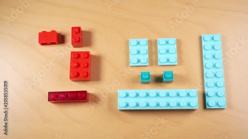 Stop motion animation of a hand selecting a red plastic building block from a colorful construction set on a wooden table, representing creativity, childhood play, and nostalgic hobbies
