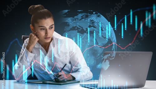 Focused businesswoman studying financial charts at desk with glowing global m...