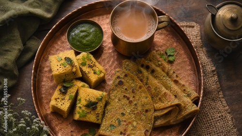 Traditional copper tray with Dhokla, Thepla, and a cup of Masala Chai from above.