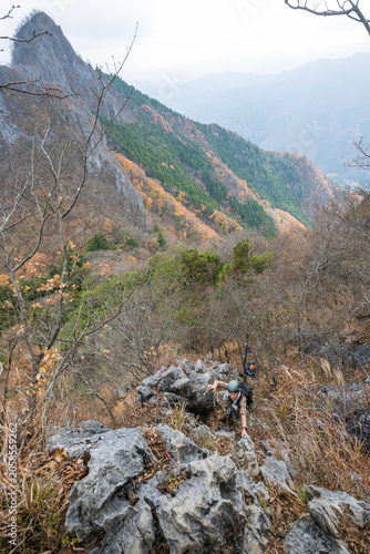 Canvas Print Hikers scrambling up rocky mountain ridge with autumn foliage and dramatic peaks
