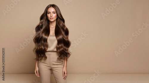 A woman with long, wavy hair extensions standing against a beige background.