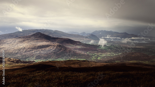 Patches of green farmland are scattered across the valley floor, contrasting with the muted tones.