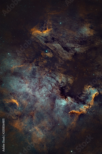 A cosmic nebula fills the frame, presenting swirling clouds of teal, orange, and dark dust against a starry background.