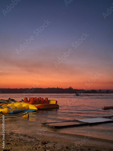 Cuadro en lienzo Vibrant orange sunset over Mekong river with inflatable water toys on shore
