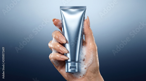 Elegant hand holds a sleek silver cosmetic tube with gentle foam, highlighting personal care and skincare hygiene in a sophisticated studio setting