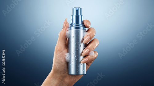 Woman hand holding a metallic blue cosmetic pump bottle with soap foam and water droplets
