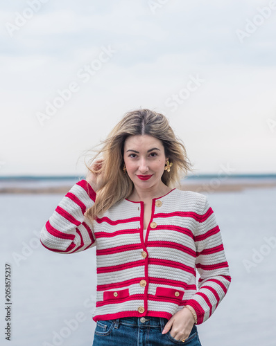 Elegant lady in red and white striped cardigan by the water. Spring lifestyle fashionable portrait