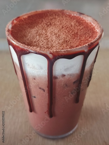 This iced drink features a pinkish base, likely strawberry, topped with white foam and a generous drizzle of chocolate syrup.