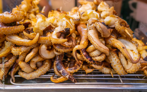 Grilled squid tentacles on metal rack at asian street food market for local culinary business and traditional seafood cuisine concept