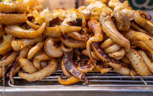 Grilled squid tentacles on metal rack at asian street food market for local culinary business and traditional seafood cuisine concept