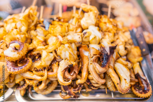 Grilled squid tentacles on metal rack at asian street food market for local culinary business and traditional seafood cuisine concept