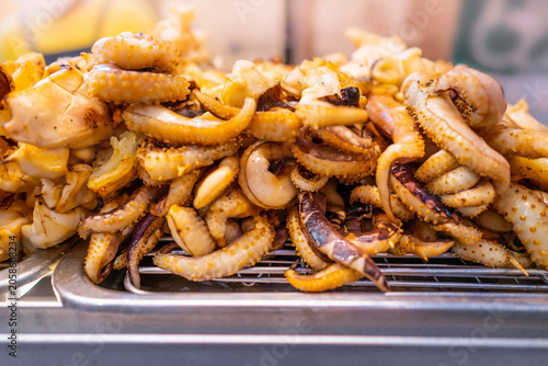 Grilled squid tentacles on metal rack at asian street food market for local culinary business and traditional seafood cuisine concept