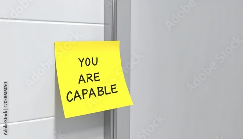 A bright yellow sticky note affixed to a white surface, stating ?YOU ARE CAPABLE.?