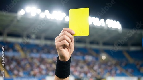 A hand holding a yellow card in a stadium