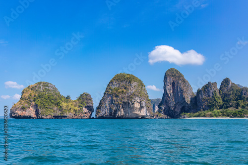 Limestone sea stack islands near the shore of Railay Beach, in Krabi, southern Thailand. Blue Andaman Sea, cloudy blue sky. 
