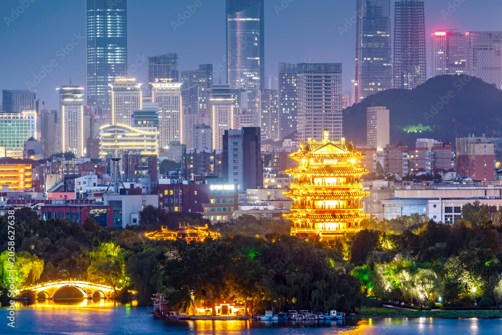 Fototapeta premium Illuminated traditional pavilion in modern city skyline at night
