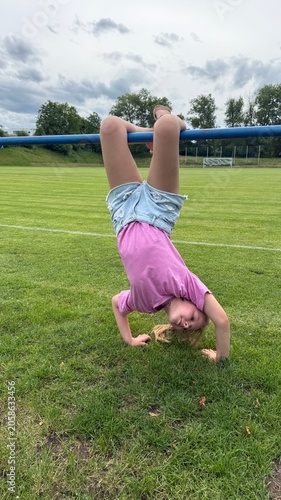 Obraz na płótnie Nine-Year-Old Girl Hanging Upside Down on a Horizontal Bar Outdoors