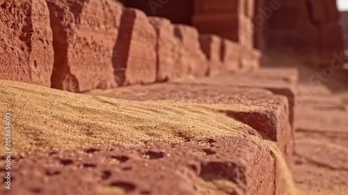Fine Golden Sand Pouring Onto Textured Red Stone Surface In Warm Sunlight