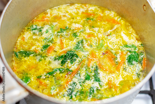 Top view of hot boiling summer stinging nettle soup with egg in a pot. Traditional green meal with fresh wild herbs closeup. Homemade rustic cooking backdrop.
