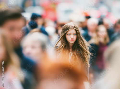 Young girl standing in crowd, long brown hair, blue eyes, solitary expression