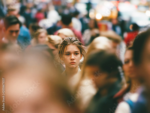 Young woman standing in a blurred crowd, thoughtful expression