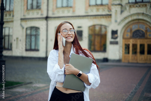 Businesswoman talking on phone outside a building while holding a notebook and wearing a white shirt