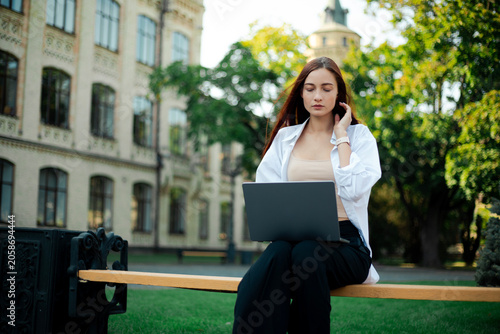 Young woman works on laptop outside at university campus in sunny weather during the day