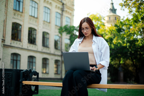 Woman works on laptop while sitting on bench in green park on sunny day