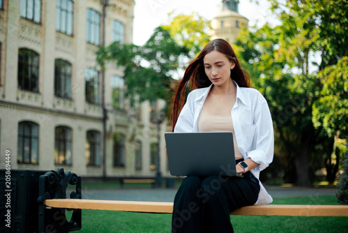 Young woman works on laptop outside at university campus in sunny weather during the day