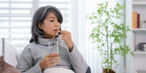 фотографія woman sitting on the sofa at home, feeling unwell, and took medicine with a glass of water to treat her illness